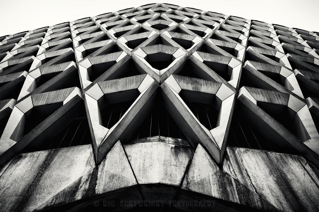 The harsh, repeating lines of the outside of a brutalist parking structure.