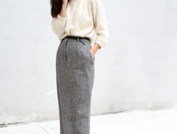 A photo of the torso of a woman with a while blouse and a long grey skirt on a white background. The picture is clean, soft, and minimal.